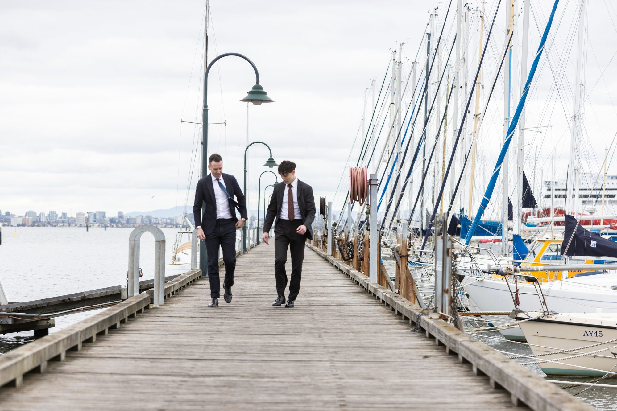 Two Compton Green agents walking the pier at Williamstown, with the Melbourne skyline behind them